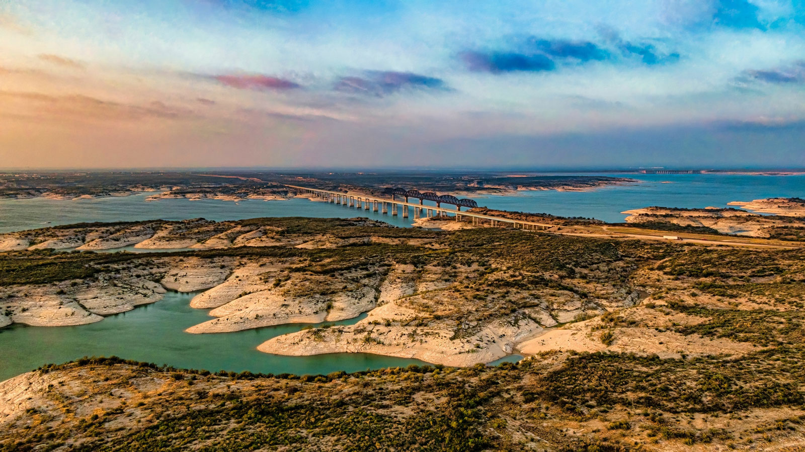 Aerial view of Amistad Reservoir with the Governor's Landing Bridge in Del Rio, Texas at sunset. Fed by the Rio Grande, Devils River, and Pecos River, water levels at Lake Amistad have been low for over a decade.
