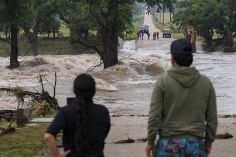 Onlookers gather on both sides as floodwaters swallow East Lane Valley Road in Comfort, Texas, on July 16, 2026. Heavy rainfall pushed the Guadalupe River out of its banks across the Hill Country. 