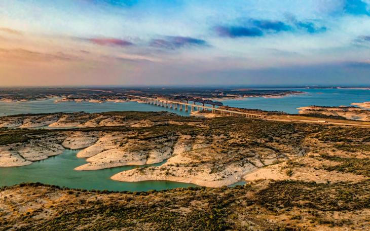 Aerial view of Amistad Reservoir with the Governor's Landing Bridge in Del Rio, Texas at sunset. Fed by the Rio Grande, Devils River, and Pecos River, water levels at Lake Amistad have been low for over a decade.